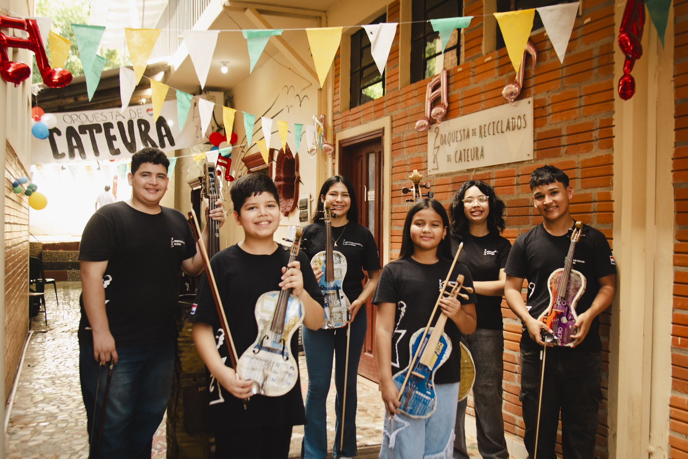 Sechs Jugendliche stehen mit ihren Instrumenten aus Müll im Hof der Musikschule von Cateura, über ihnen bunte Wimpel